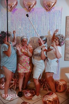 three women pose for a photo in front of balloons and streamers with their hands up