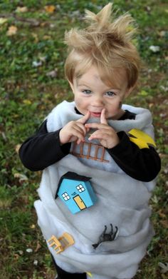 a little boy dressed in a costume standing on the grass with his finger to his mouth