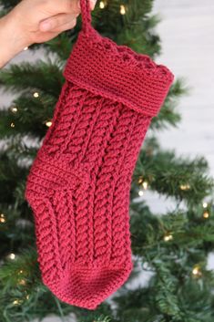 a hand holding a red knitted stocking in front of a christmas tree