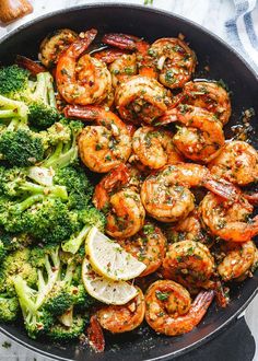 shrimp and broccoli in a skillet with lemon wedges on the side