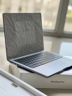 an open macbook pro laptop sitting on top of a box next to a window