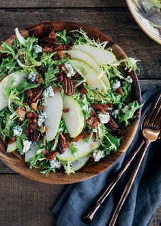 a salad with apples, pecans and blue cheese in a wooden bowl on top of a table