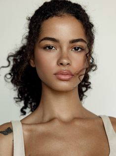 a close up of a woman with curly hair and tattoos on her chest, looking at the camera