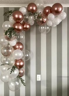 some balloons and greenery are hanging from the wall in front of a striped wall