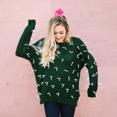 a woman wearing a green sweater with white arrows on it and pink wall in the background