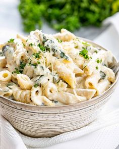 a white bowl filled with pasta and spinach on top of a table next to some parsley