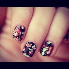 a woman's hand with black and pink flowers on it, holding onto her nails