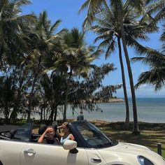 two women are sitting in the back of a convertible car with palm trees behind them