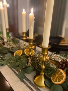 candles are lit on a table with greenery and orange slices