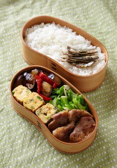 two bento boxes filled with food on top of a green tablecloth covered bed