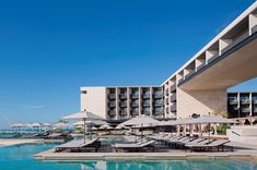 an outdoor swimming pool with lounge chairs and umbrellas in front of the beach resort