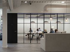 an office with people sitting at desks and working on laptops in front of glass walls