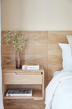 a bed with white sheets and pillows next to a night stand with flowers on it