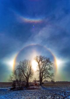 two rainbows are seen in the sky over a snow covered field with trees and grass