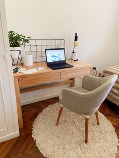 a laptop computer sitting on top of a wooden desk next to a chair and potted plant