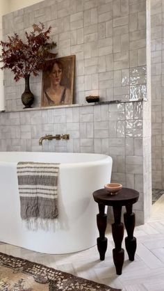 a white bath tub sitting in a bathroom next to a table with a vase on it