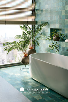 a bath tub sitting next to a window in a room with blue tiles on the walls