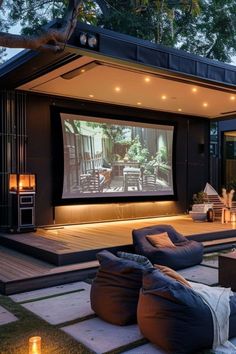 an outdoor movie theater is lit up with candles and lights on the ground, while two large bean bags sit in front of it