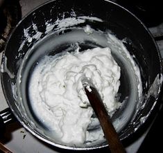 a metal pan filled with white food on top of a stove next to a wooden spoon