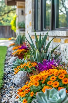 an assortment of flowers and rocks in front of a house