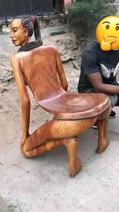 a man sitting on the ground next to a wooden chair with two heads carved into it