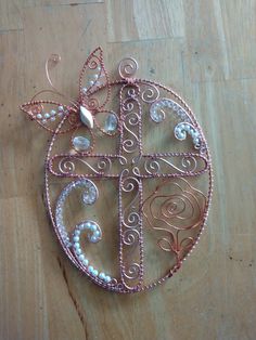 a cross made out of wire and pearls on a wooden table with a butterfly hanging from it