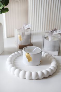 a white candle with gold leaf on it sitting in front of two small glass boxes