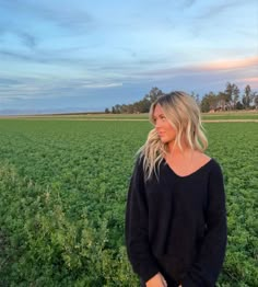 a woman standing in the middle of a green field with her hands on her hips