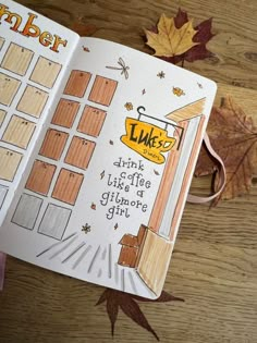 a hand holding an open planner book on top of a wooden table next to leaves