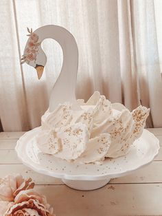 a swan shaped cake sitting on top of a white plate next to a pink flower