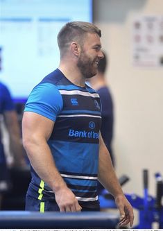 a man standing in front of a table wearing a blue and white shirt with the bank of england logo on it