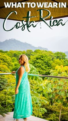 a woman in a blue dress standing on a balcony with the words what to wear in costa rica