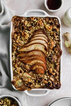 a white dish filled with sliced apples and granola on top of a table next to bowls of fruit