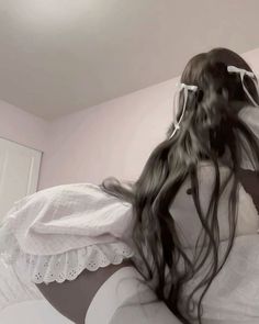 a woman with long black hair is sitting on a white bed and has her back turned to the camera