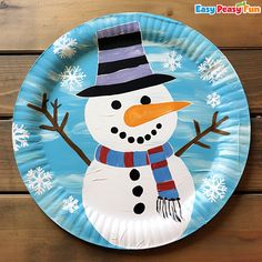 a paper plate with a snowman painted on the front and sides, sitting on a wooden surface