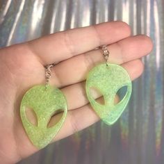 a hand holding two green alien shaped earrings