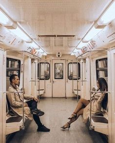 two people sitting on a subway car with their legs crossed and looking at each other