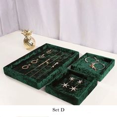 three green velvet jewelry boxes sitting on top of a white table next to a gold pineapple