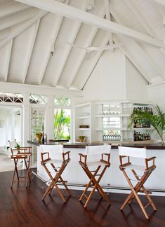 a kitchen with white walls and wooden flooring next to an open area that has several chairs in it