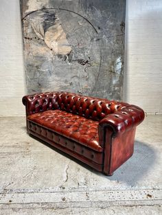 a brown leather couch sitting in front of a wall with a painting on it's side