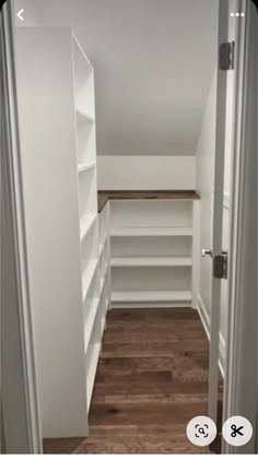 an empty walk in closet with white shelving and wood flooring on the walls