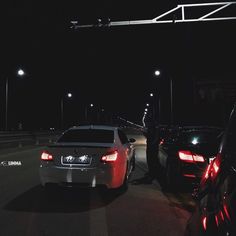 two cars parked on the side of a road at night with street lights in the background