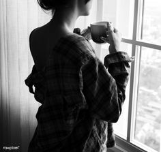 a woman is holding a cup and looking out the window