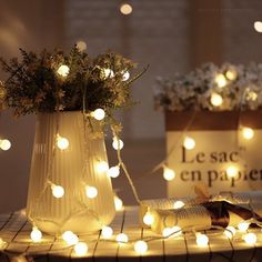 two vases filled with flowers and lights on top of a wooden table next to each other