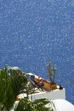 a person is lounging on the roof of a building overlooking blue water and palm trees