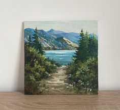 a painting of a path leading to a lake with mountains in the distance and pine trees on either side