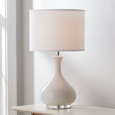 a white lamp sitting on top of a table next to a wooden cabinet and window