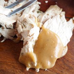 a wooden table topped with meat and gravy next to a fork on top of it