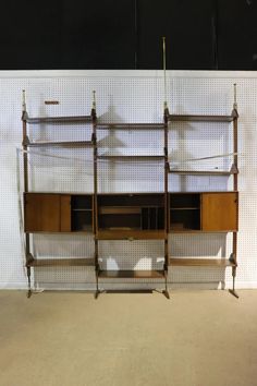 a wall mounted shelf with three shelves and two hooks on each side, in front of a white wall