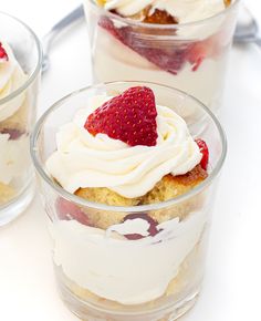 three desserts with strawberries and whipped cream in small glass dishes on a white surface